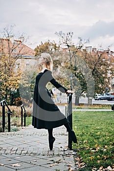 Ballerina Dancing in autumn city street, Modern Ballet Dancer in black dress, Pointe Shoes outdoors. Ballerina stretches