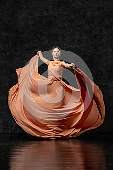 Ballerina dancing in a long peach dress on a black background.