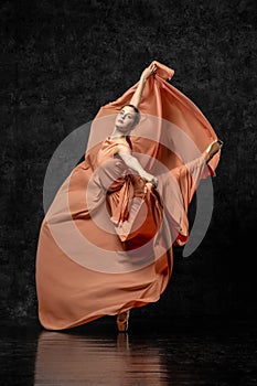 Ballerina dancing in a long peach dress on a black background.