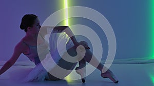 Ballerina demonstrates her flexibility in the studio against a backdrop of colorful neon lights. The dancer, sitting on