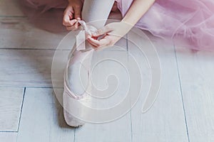 Ballerina hands puts pointe shoes on leg in dance class