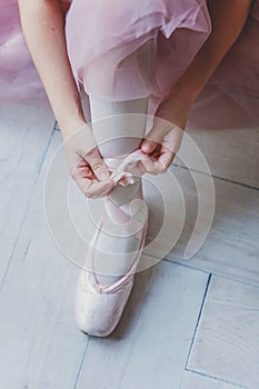 Ballerina hands puts pointe shoes on leg in dance class