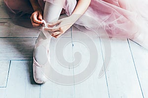 Ballerina hands puts pointe shoes on leg in dance class