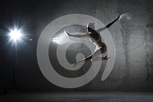 Ballerina in a jump with flour on a gray background.