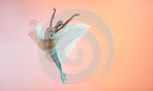 Ballerina in a light light dress flying in jump on an illuminated colored background