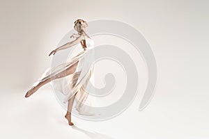 Ballerina in maxi dress dancing over light studio background. Ballet Dancer. Modern Dance. Graceful Woman. Hobby