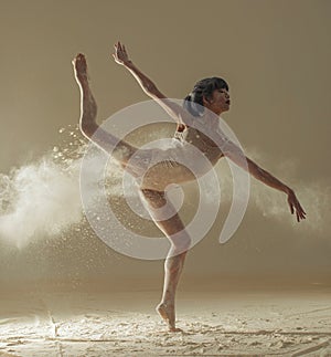 Ballerina performs arabesque pose against background of white flour cloud in air