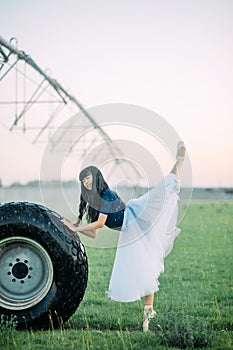 Ballerina performs swallow pose on farm near the wheel of agricultural sprayer
