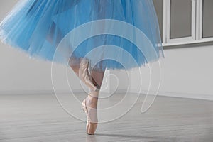 Ballerina in pointe shoes and light blue skirt dancing indoors, closeup