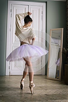 ballerina poses showing her legs in the room in front of the mirror in pointe shoes and tutu