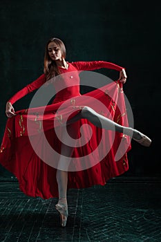 Ballerina posing in pointe shoes at black wooden pavilion