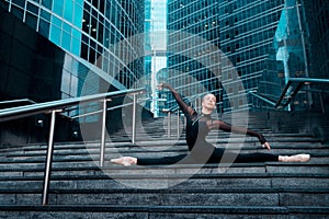 The ballerina is sitting on the splits. City street background