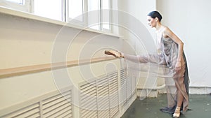 Ballerina in stage dress stretching leg in vertical split near window in class