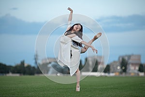 Ballerina stands in pose of swallow on lawn.