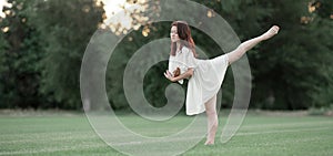 Ballerina stands in pose of swallow on lawn.