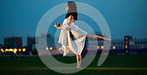 Ballerina stands in pose of swallow on lawn in evening.