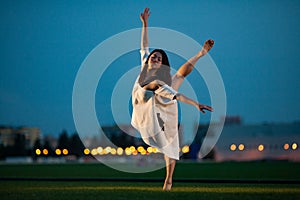 Ballerina stands in pose of swallow on lawn in evening.