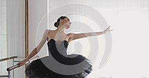 Ballerina stretches on bar, graceful girl practicing ballet in the Studio