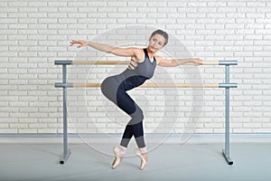 Ballerina stretches herself near barre at ballet studio, full length portrait.