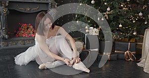 Ballerina ties up pointes sitting in a Christmas decorated room