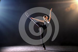 Ballerina in tight-fitting suit is dancing on black background on pointe shoes, silhouette is illuminated by sources of color