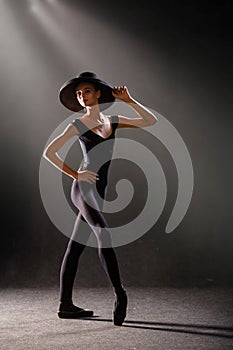 Ballerina in tight-fitting suit is dancing on black background on pointe shoes, silhouette is illuminated by sources of color