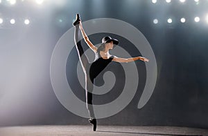 Ballerina in tight-fitting suit is dancing on black background on pointe shoes, silhouette is illuminated by sources of color