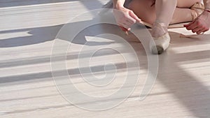 Ballerina in tutu sitting on the floor and tying pointe shoes