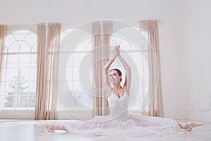 A ballerina on a twine in white clothes in a white studio.