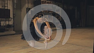 Ballerina tying pointe ballet shoes on stage.