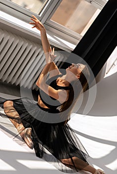 Ballerina wearing black dress sitting on floor dancing with light.