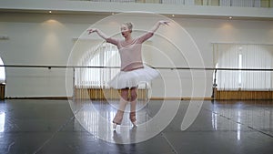 Ballerina in white ballet tutu dress practicing in dance studio or gym. Woman dancing classical pas in class. Alone