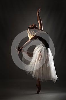 Ballerina with a white dress and black top posing on gray background photo