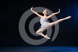 Ballerina in a white dress flying in a jump on black background