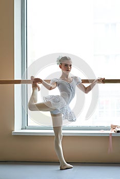 Ballerina in white dress posing at barre.