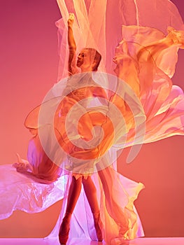 Ballerina. Young graceful female ballet dancer dancing over red studio. Beauty of classic ballet.