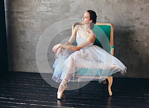 Ballet dancer ballerina in beautiful light blue dress tutu skirt posing sitting on vinage chair in loft studio