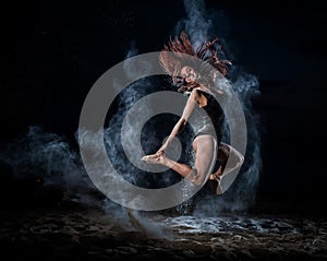 Ballet dancer in black bodysuit jumps high and dance with flour on the beach in the evening. Women`s street ballet