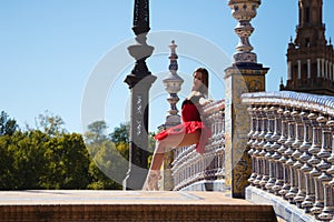 Ballet dancer with red tutu leaning on a park railing in seville. The dancer makes different postures and stretches on the railing