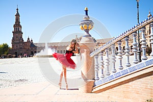 Ballet dancer with red tutu leaning on a park railing in seville. The dancer makes different postures and stretches on the railing