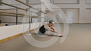 Ballet dancer in training suit stretches legs