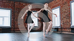 Ballet dancing indoors - two little gymnastics girls synchronously dancing in black suit on training