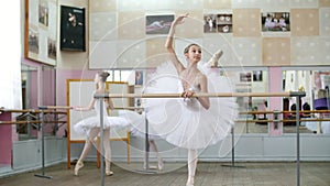 In the ballet hall, girl in white ballet tutu, pack is engaged at ballet, rehearse attitude, raises her leg up behind