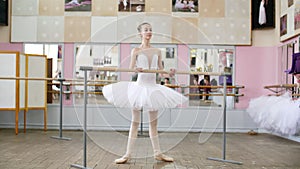 In the ballet hall, girl in white pack is engaged at the ballet, rehearse Roleve, goes up on toes, in pointe shoes