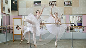 In ballet hall, girls in white ballet skirts are engaged at ballet, rehearse attitude, Young ballerinas standing on toes