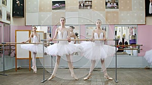 In the ballet hall, girls in white ballet tutus, packs are engaged at ballet, rehearse plie forward, Young ballerinas