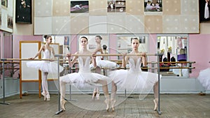 in the ballet hall, girls in white ballet tutus, packs are engaged at ballet, rehearse plie forward, Young ballerinas