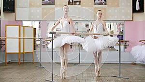 In the ballet hall, two girls in white ballet tutu, packs are engaged at ballet, rehearse pas de bourre, Young