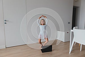 Ballet lesson online. Little girl dancing while looking at computer at home.