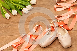 Ballet pointe shoes and white tulips on wooden background